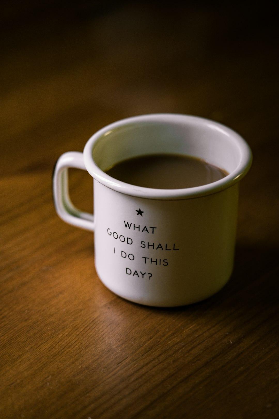Coffee mug with words "What good shall I do this day?" sitting on a wooden surface.